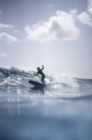 Dynamic surfboarding under bright sky with rolling waves and clear view of the ocean.