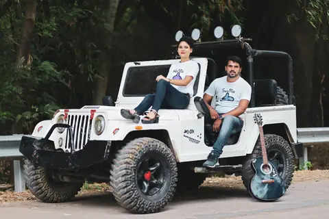 A young couple sitting on a jeep with a guitar, enjoying a road trip adventure.
