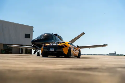 A sleek sports car parked next to a private jet under a clear sky at an airport.