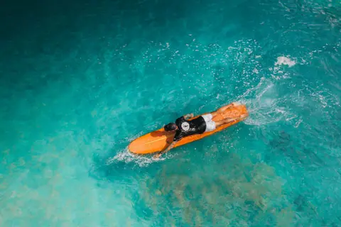 Top-down shot of a surfer paddling on a vibrant turquoise sea, showcasing summer adventure.