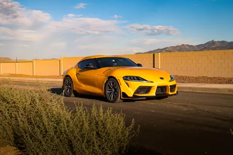 A vibrant yellow sports car parked on a desert road under a clear blue sky.