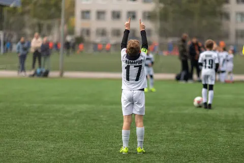 A young soccer player raises hands in celebration on an outdoor field.