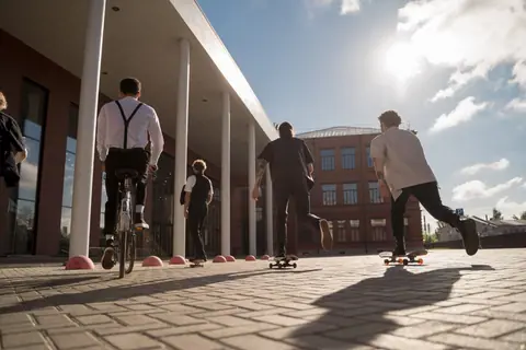 Four people skateboarding and biking outdoors near a modern building during the day.