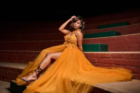 A woman wearing a stunning yellow gown seated on red steps, exuding elegance and charm.