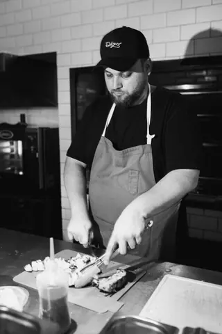 A chef wearing an apron and cap prepares food on a kitchen counter.