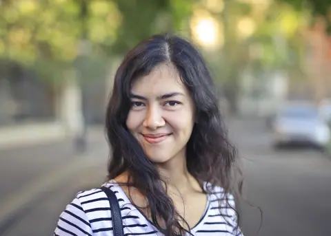 Young woman with brunette hair smiling outdoors on a sunny day.