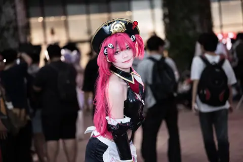 Vibrant cosplay character with pink hair at an indoor anime convention.