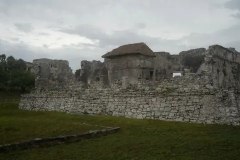 A stunning view of ancient stone ruins surrounded by lush greenery under a cloudy sky.