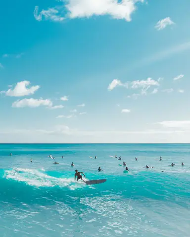 Aerial view of surfers enjoying a sunny day on turquoise waves with a clear blue sky.