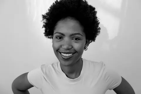 Black and white portrait of a smiling woman with curly hair wearing a white top.