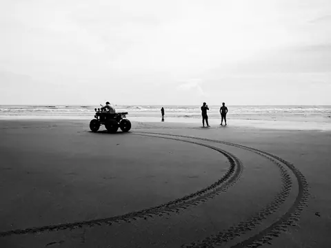 Monochrome scene of an ATV and people on the sands of Cox's Bazar beach in Bangladesh.