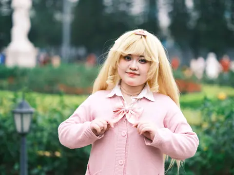 A cosplayer in a pink outfit poses in a lush green park, creating a vibrant, playful scene.