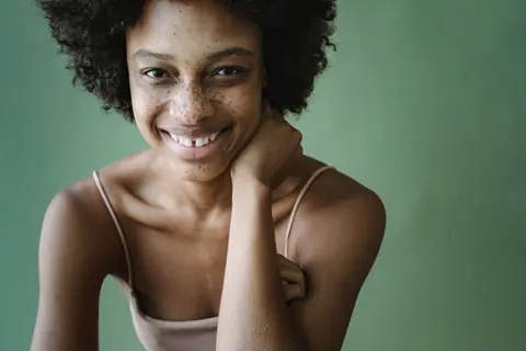 Close-up portrait of a smiling woman with afro hair against a green background.
