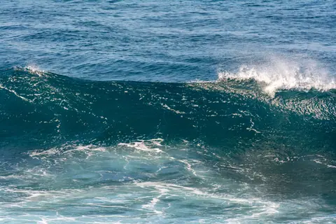 Dynamic ocean wave captured with spray and foam under bright daylight conditions.