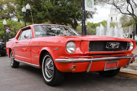 Vintage red Ford Mustang parked in a city with fountain backdrop, capturing classic car elegance.