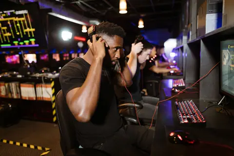 Focused gamers with headphones immersed in PC games at a lively esports venue.