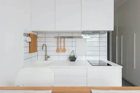 Wooden table placed near white cupboards in modern kitchen with minimalist interior in daylight