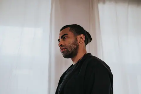 Side view portrait of a man with dreadlocks standing indoors looking serene and serious.
