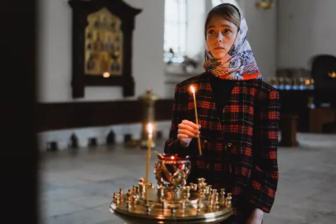 Teenager holding a candle in an Orthodox church, exemplifying spirituality and introspection.