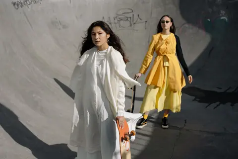 Two stylish women posing with skateboards in a skate park.