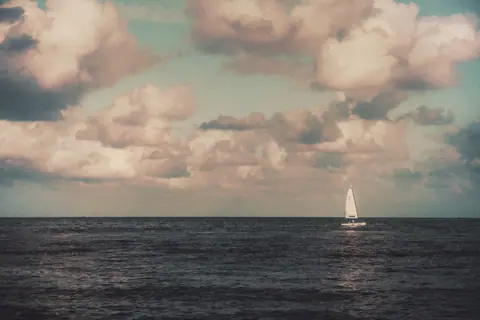 A peaceful seascape featuring a solitary sailboat under a dramatic sky in Cancun, Mexico.