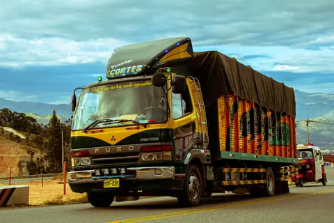 Vibrant cargo truck cruising a scenic mountain highway under a dramatic sky.