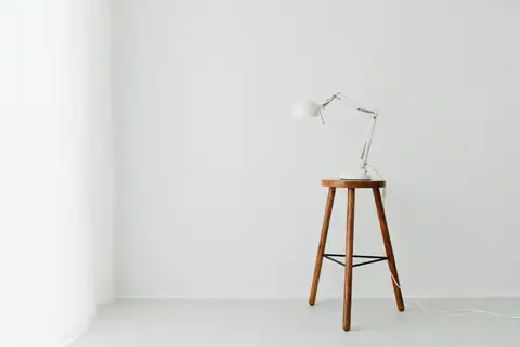 Simple minimalist setup with a white desk lamp placed on a wooden stool against a white wall.