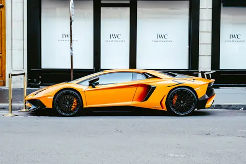Side view of a vibrant orange Lamborghini Aventador parked in an urban setting, showcasing its luxury and design.