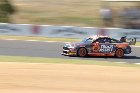 A racing car speeds around Mount Panorama track, showcasing dynamic motion and precision.