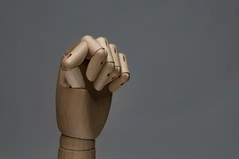 Detailed wooden mannequin hand showing a fist with a gray backdrop.