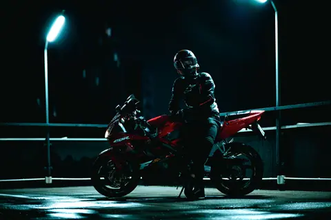 Motorcyclist on a red bike under streetlights at night.