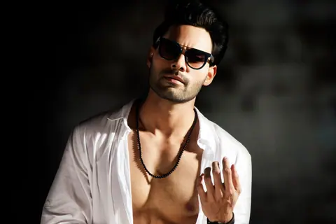Portrait of a stylish man in sunglasses and an open shirt posing confidently with dramatic lighting.