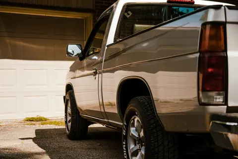 A silver pickup truck parked in a sunny residential driveway with closed garage doors.