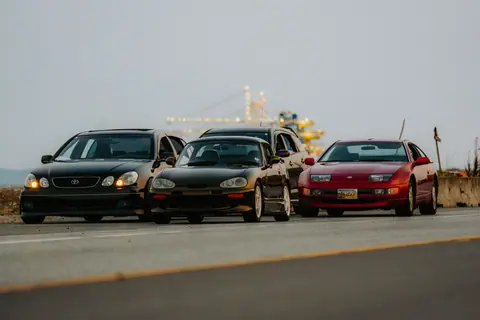 Four classic sports cars line up on a scenic road, ready for adventure.