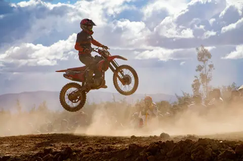 A thrilling scene of a biker catching air during an off-road motorcycle race, surrounded by a dusty landscape and spectators.