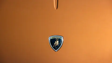 Close-up of Lamborghini emblem on sleek orange car hood.