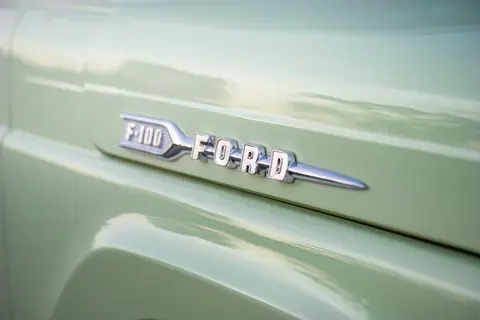 Close-up view of a vintage Ford F-100 emblem on a pastel green vehicle, ideal for automotive enthusiasts.