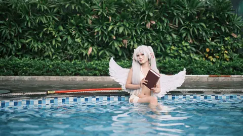 A fantasy-inspired cosplay character with angel wings holding a book by the pool.