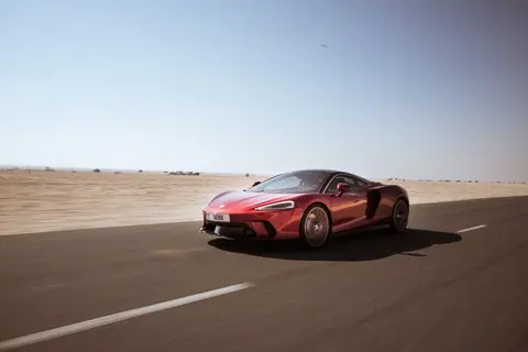 A sleek red sports car racing along a deserted highway under a clear blue sky.