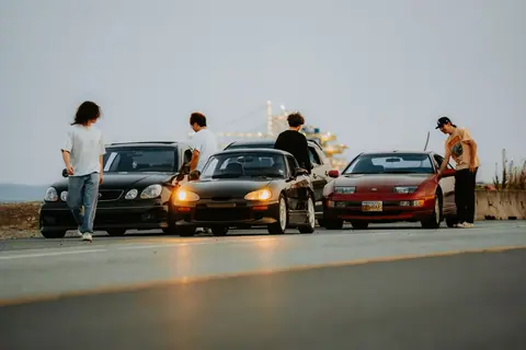 Young adults gather around sports cars in an urban setting, showcasing car culture.
