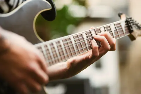 Detailed shot of a guitarist's hand playing an electric guitar outdoors.