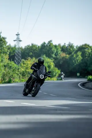 Dynamic shot of a motorcyclist riding through a forested curved road, conveying speed and freedom.