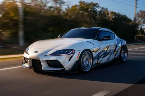 A sleek white sports car with custom graphics speeds on an open road, showcasing dynamic motion.