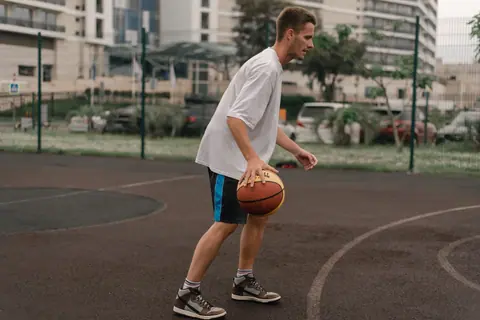 A young adult practicing basketball outdoors on an urban court, focusing on dribbling skills.