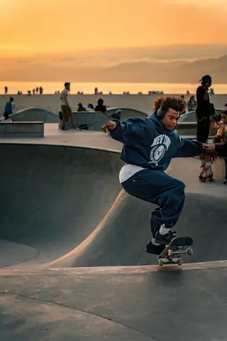 Skateboarder performing tricks with headphones at Venice Beach skatepark during sunset in Los Angeles.