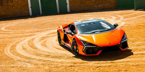 Vibrant orange sports car parked in a sunlit dirt track, showcasing luxury design.