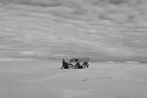 A Land Rover Defender with a man on a vast and isolated beach in Warriewood, Australia.