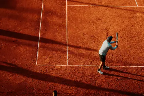 Aerial view of a tennis player preparing a swing on a clay court during daytime.