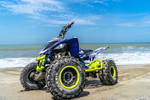 A quadbike parked on a sandy beach with the ocean and clear blue sky in the background.