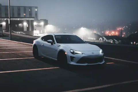 A sleek white sports car in a dimly lit urban parking lot at night, exuding a modern and bold vibe.